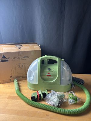 une photo d'un aspirateur vert et blanc posé sur une table, à côté d'une boîte