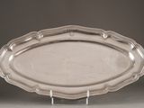 an oval silver platter on a stand on a gray surface