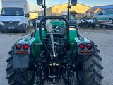 un tracteur vert garé sur un parking, avec d'autres véhicules en arrière-plan