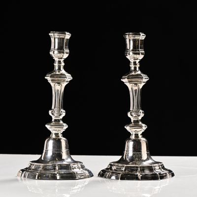 une paire de bougeoirs en argent posés sur une table blanche, sur fond noir