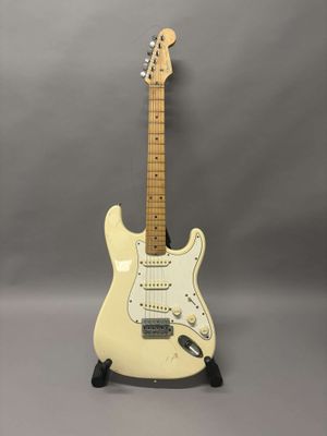 une guitare électrique blanche posée sur un support, sur fond gris