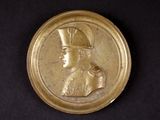 une image représentant une assiette en or sur laquelle figure le portrait d'un homme coiffé d'un chapeau