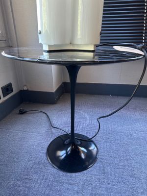 une table en verre avec un piètement noir, sur laquelle est posé un vase blanc