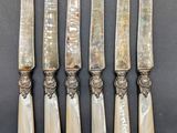 five silverware knives with mother of pearl handles on a black surface