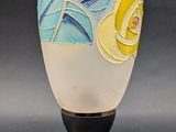 a white vase with a yellow flower on it next to a spoon