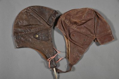 pair of brown leather aviator ' s hats on a gray surface