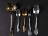 six spoons and a fork are arranged in a row on a black surface