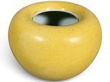 a yellow vase with a hole in it on a white surface