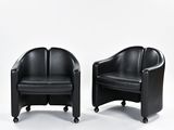 pair of black leather lounge chairs on casteors against a white background