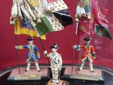 three figurines of soldiers holding flags under a glass dome