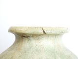 a green vase sitting on a table with a white wall in the background