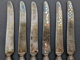 five silverplated knives are lined up on a black surface