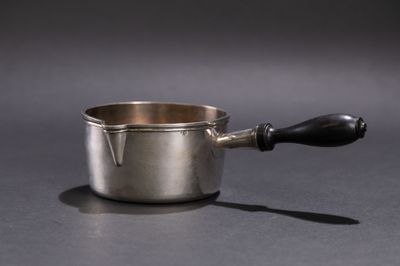 une saucière en argent avec une poignée noire posée sur une table
