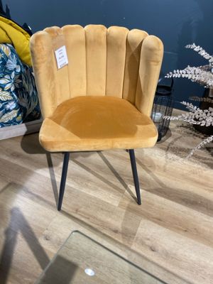 une chaise en velours jaune aux pieds noirs, dans une pièce aux murs bleus, avec une table en verre