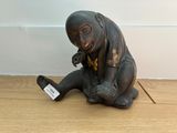 a statue of a monkey sitting on the floor holding a cell phone