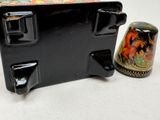 a small black box with a black lid next to a small black container with a red horse on it
