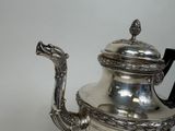 a silver tea pot with a dragon handle on a table