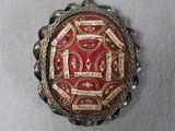 une photo d'une broche rouge et dorée posée sur un tissu blanc