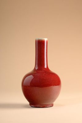 un vase rouge posé sur une table, sur fond beige