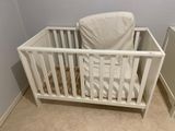 a white crib with a white sheet on it in the corner of a room