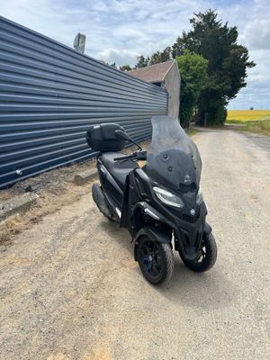 Le scooter est garé sur le bord de la route, à côté d'un immeuble.