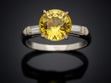 a close up of a yellow sapphire and diamond ring on a black surface