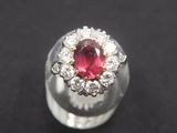 a close up of a ring with a red stone surrounded by white diamonds