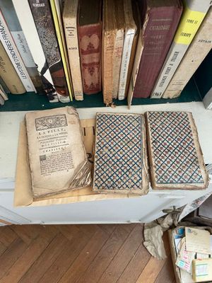 Plusieurs vieux livres sont empilés sur une table devant une bibliothèque.