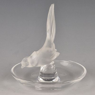 un oiseau en verre posé sur une assiette en verre posée sur une table