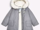 La veste est grise et blanche, avec une capuche et un col doublé de fourrure.