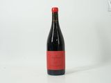 the bottle of red wine is sitting on a white surface