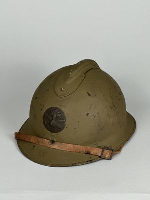 un vieux casque militaire muni d'une lanière en cuir, posé sur une surface blanche