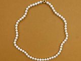 a white pearl necklace with a gold clasp on a brown background