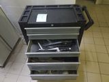 une boîte à outils noire contenant des outils, posée sur un sol carrelé