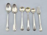 six cuillères en argent et une fourchette sont alignées sur une table