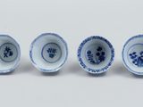 four blue and white bowls with flowers in them on a white surface