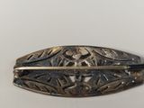 a silver brooch with a black handle on a table