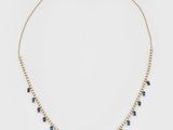 un collier en or orné de cristaux bleus et de perles sur fond blanc