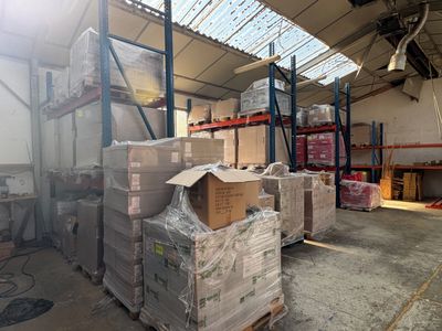 Les cartons sont empilés sur des palettes dans un entrepôt surmonté d'une verrière.