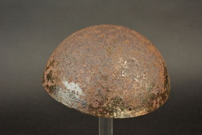 a rusted helmet on a metal stand against a black background