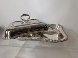 a silver plate with a silver cover on a glass table