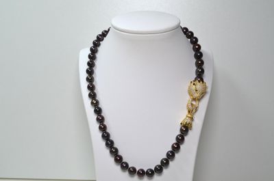 collier en perles noires et dorées orné d'un pendentif en forme de feuille dorée