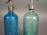 une paire de bouteilles en verre bleues et vertes, munies de poignées argentées, posées sur un support gris