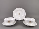 trois assiettes et tasses blanches ornées de bordures dorées sur un fond gris