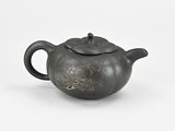 an old black teapot sitting on top of a white surface