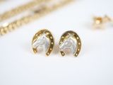 gold horse head stud earrings with a chain on a white surface