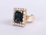 a close up of a ring with an emerald stone surrounded by diamonds