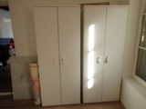 two white cupboards in the corner of a room with a window