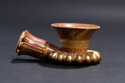 un vase doré muni d'une anse marron, posé sur une surface noire