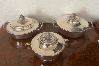 three silver dishes on a wooden table with a white wall in the background